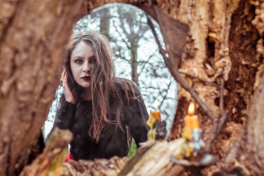 mystical woman looks in the mirror near a tree at the spring forest