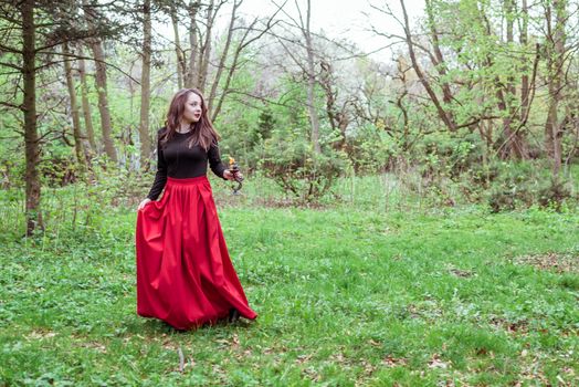 mystical witch woman in a red skirt with a candle in spring forest