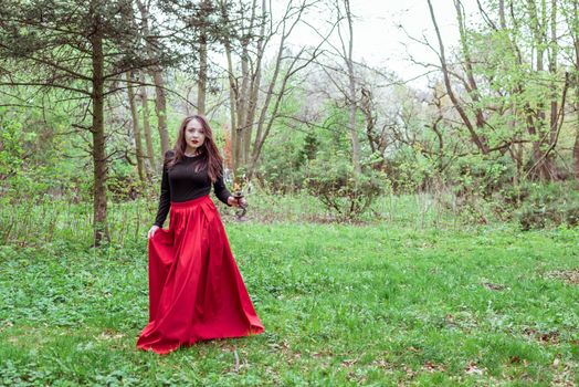 mystical witch woman in a red skirt with a candle in spring forest