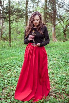 mystical witch woman in a red skirt with a candle in spring forest