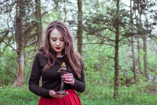 mystical witch woman in a red skirt with a candle in spring forest