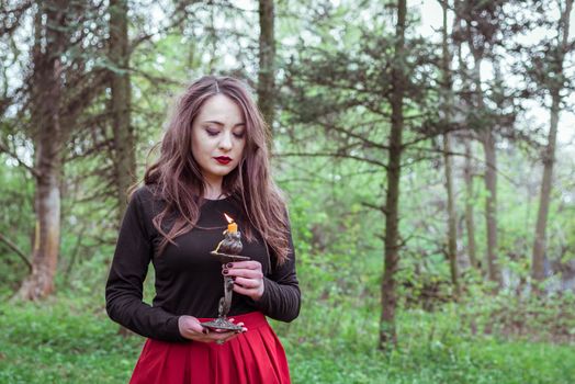 mystical witch woman in a red skirt with a candle in spring forest