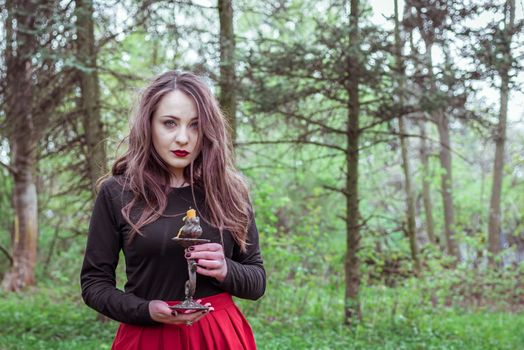 mystical witch woman in a red skirt with a candle in spring forest
