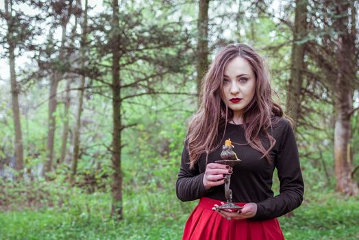 mystical witch woman in a red skirt with a candle in spring forest