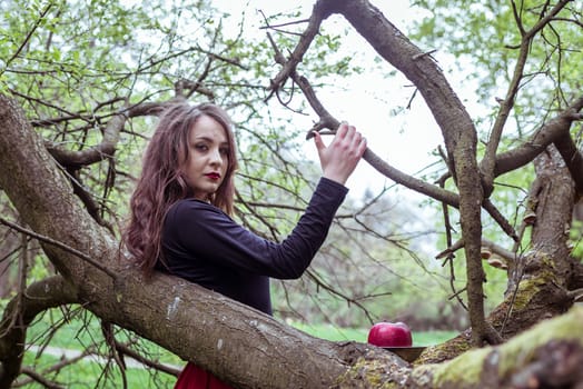 close-up beautiful woman in a red dress standing near a tree in the forest