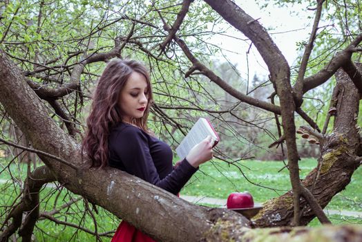 woman reading a book near a tree in the spring forest