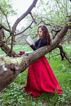 woman reading a book near a tree in the spring forest