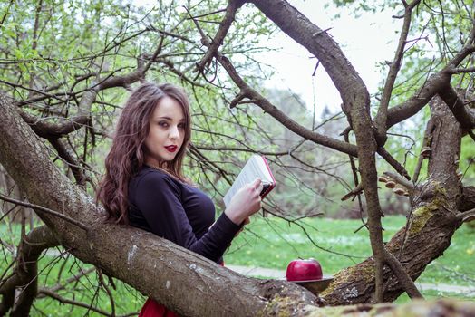 woman reading a book near a tree in the spring forest