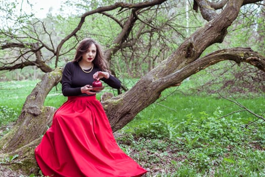 girl in a red skirt sitting on a tree trunk with apple in hand