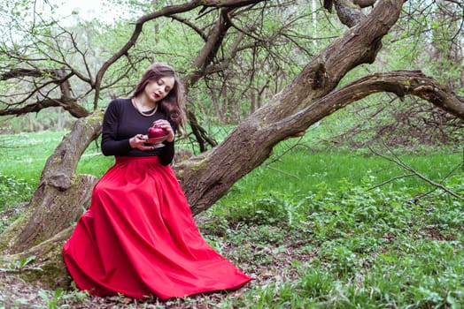 girl in a red skirt sitting on a tree trunk with apple in hand