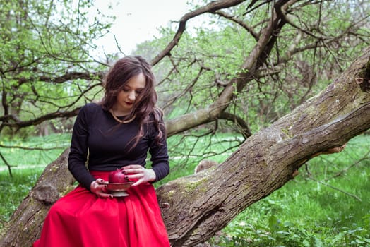 girl in a red skirt sitting on a tree trunk with apple in hand