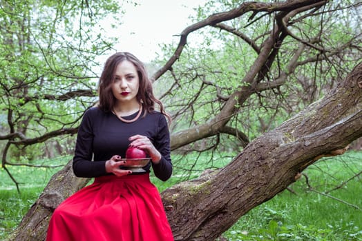 girl in a red skirt sitting on a tree trunk with apple in hand