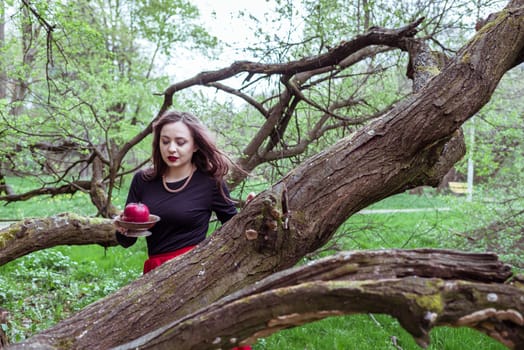 girl in a red skirt standing near a tree trunk with apple in hand