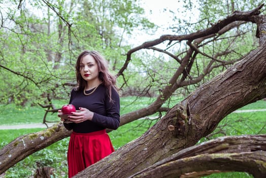 girl in a red skirt standing near a tree trunk with apple in hand