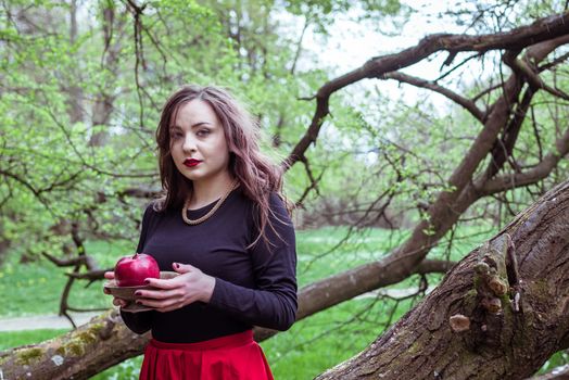 girl in a red skirt standing near a tree trunk with apple in hand