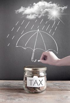 Umbrella being sketched on a chalkboard protecting a jar of tax savings