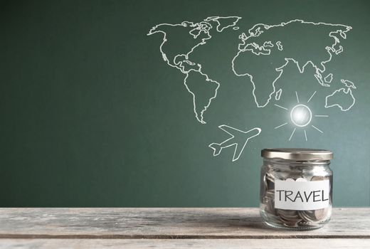 Travel savings jar by a chalkboard with a world map
