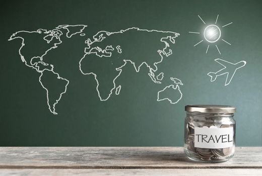 Travel savings jar by a chalkboard with a world map