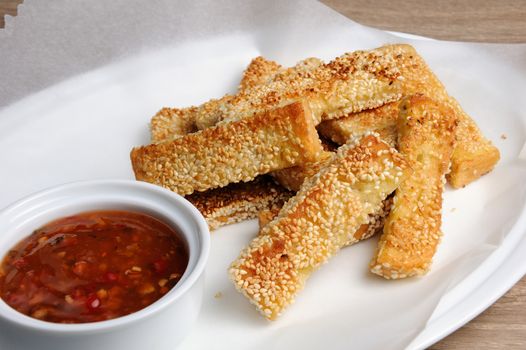 Slices of toast fried in breaded with cheese , sesame and sauce on a paper  in   plate 