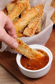 Slice of toast roasted in breaded with cheese and sesame slipped in a sauce on a wooden board