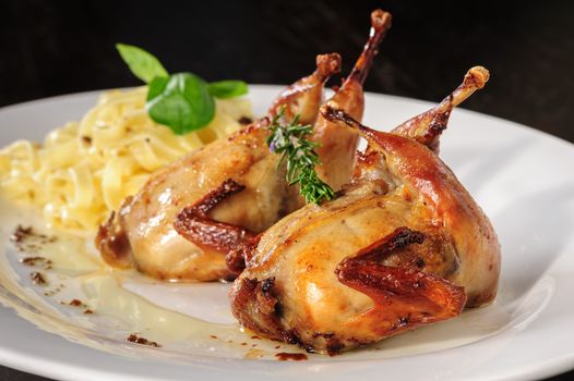 Rosted or fried quail with herbs and tagliatelle at white plate on wooden table
