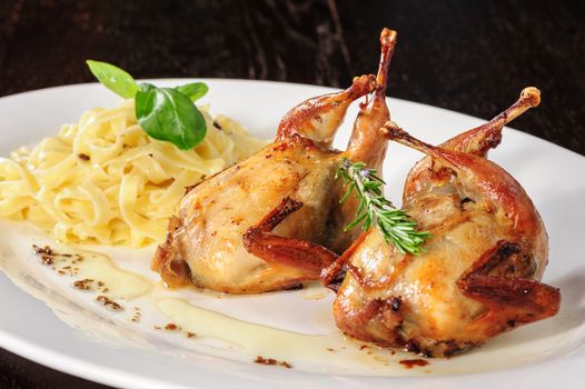 Rosted or fried quail with herbs and tagliatelle at white plate on wooden table