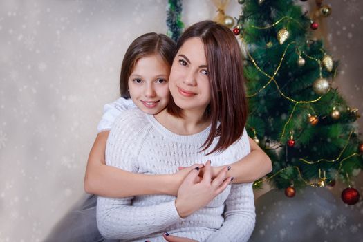 Adorable mother and daughter hugging under Christmas tree