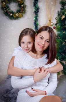 Cute daughter and mother embracing under Christmas tree