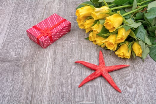 Yellow roses, red gift and red starfish on grey wooden background