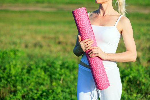 Yoga woman with a carpet posing outdoors