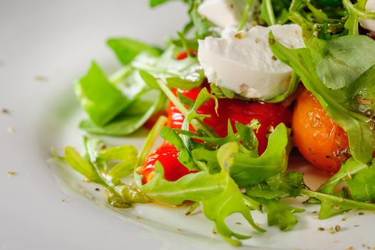 Warm salad with Tomatoes, ruccola, spinach, cooked bell pepper and cheese served on white plate