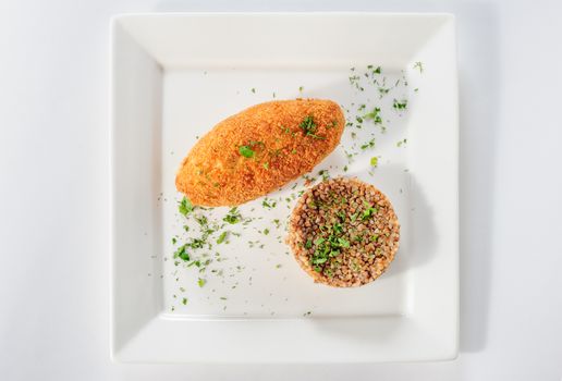 Big cutlet of turkey meat with garnish made of buckwheat cereal, top view
