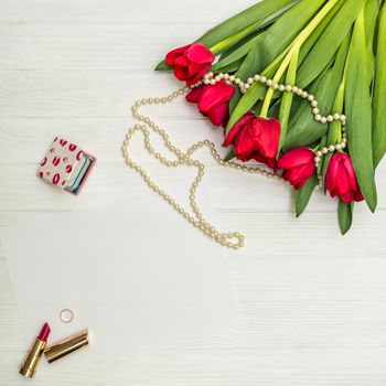 red tulips in the necklace, lipstick, one ring and a white sheet of paper on the background of white wooden board