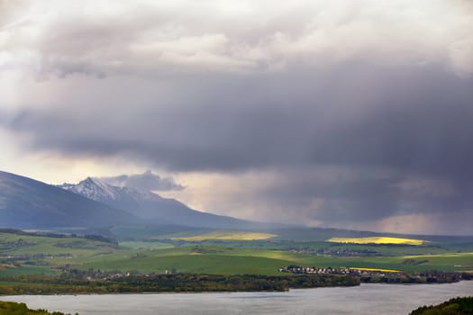 Town on the lake behind the foothills. Spring rain and storm in mountains. Green spring hills of Slovakia. Spring stormy scene.