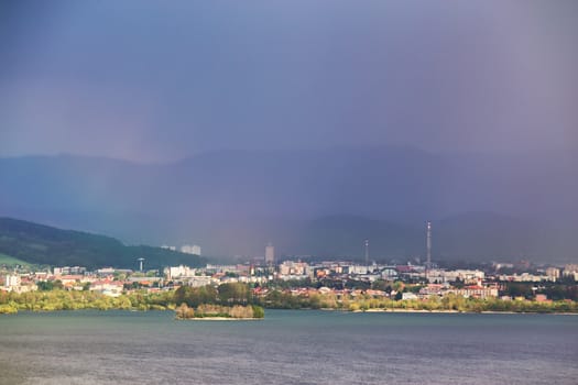 Town on the lake behind the foothills. Spring rain and storm in mountains. Green spring hills of Slovakia. Spring stormy scene.