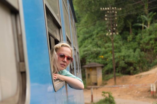 Blonde caucasian woman looking trough old retro blue train window , traveling by train in third world country.