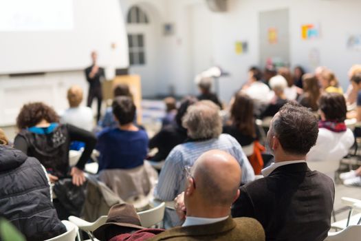 Business and entrepreneurship symposium. Speaker giving a talk at business meeting. Audience in the conference hall. Rear view of unrecognized participant in audience.