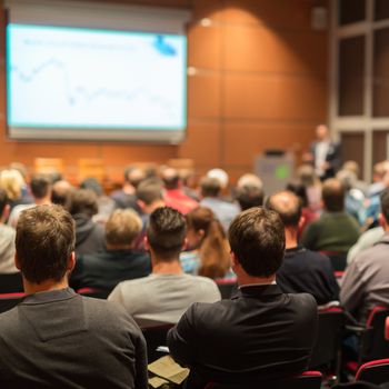 Speaker Giving a Talk at Business Meeting. Audience in the conference hall. Business and Entrepreneurship. Focus on unrecognizable people from rear.