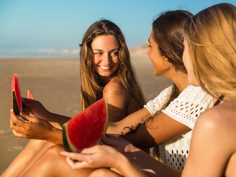 Best friends having fun on the beach and eating watermelon