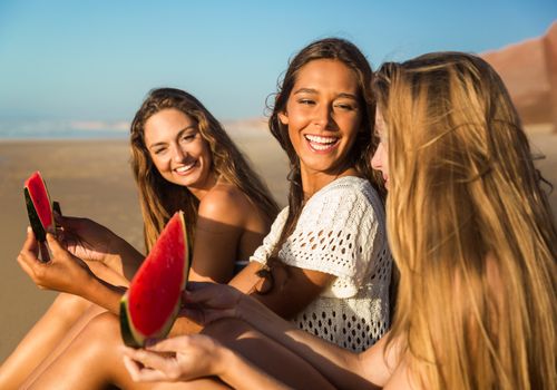 Best friends having fun on the beach and eating watermelon