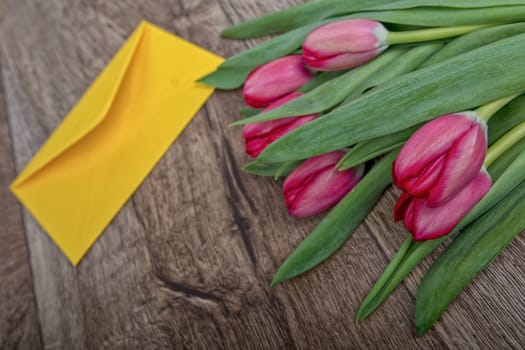 Envelope and red tulip on a wooden background