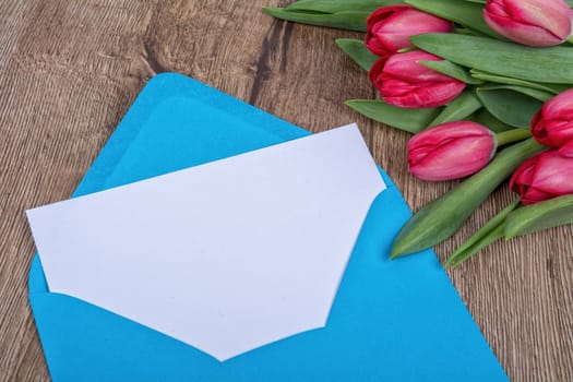 Envelope with sheet of paper and red tulips on a wooden background