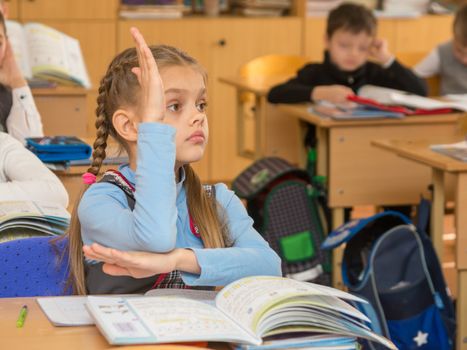 Girl schoolgirl at a lesson at school wanting to pull your hand up to answer a question