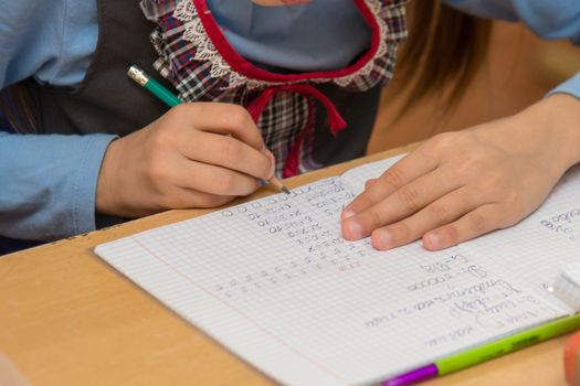 First-grader at a lesson mathematics writes in the notebook, close-up