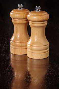 Two wooden pepper mills at dark table surface