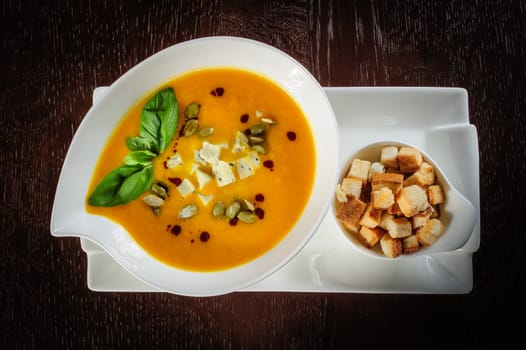Roasted pumpkin soup with cream and pumpkin seeds on dark wooden background. Top view.