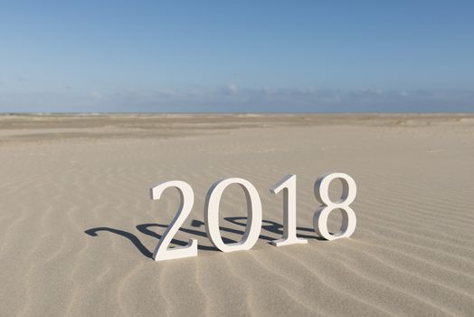 White wood figures on a beach forming the text two thousand eighteen as conceptual welcoming of the coming new year
