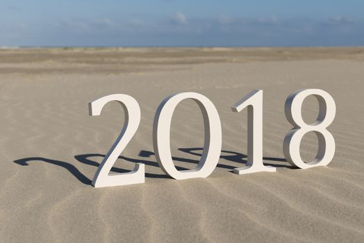 White wood figures on a beach forming the text two thousand eighteen as conceptual welcoming of the coming new year
