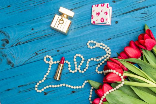 red tulips in the necklace, lipstick and bottle of perfume on the background of blue wooden board