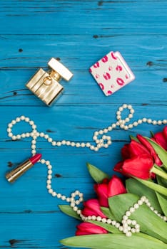 red tulips in the necklace, lipstick, one ring and a white sheet of paper on the background of blue wooden board